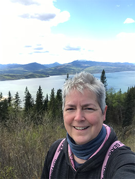 Woman with short white hair smiling in front of lake view.