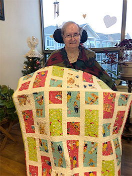 Woman sitting in front of window showing off a yellow quilt