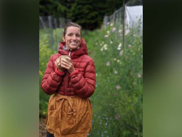 a woman in a red coat stands in a green field holding a cup of coffee