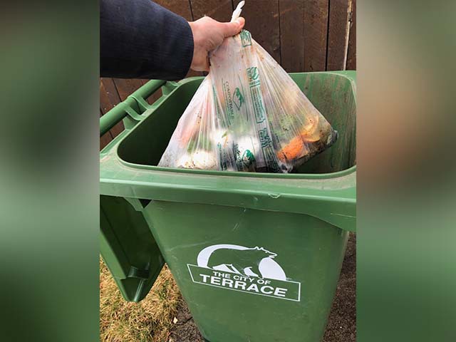 a hand is seen placing compost into a large green compost bin