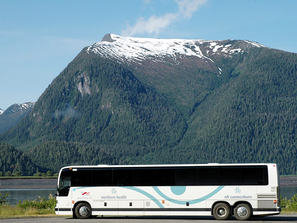 A charter bus is parked in front of a river and mountain range.