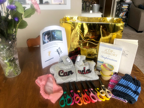 Two books, a Canada hoodie, different coloured scissors, and toques are unpacked on a wood table. 