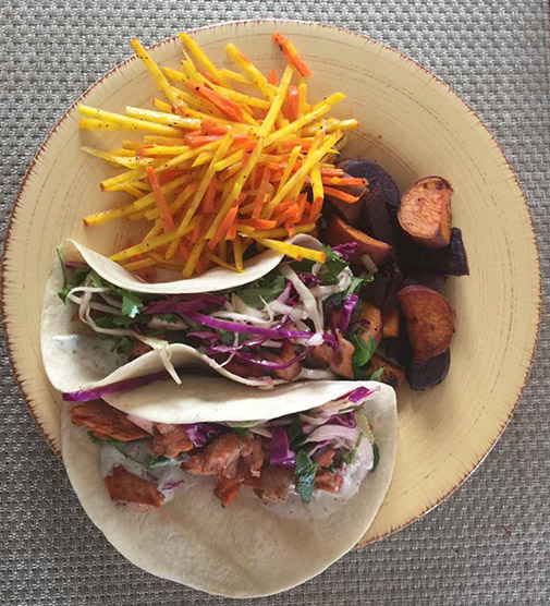 2 tacos on a plate with vegetables and fish.