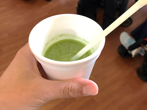 A hand holds a styrofoam cup filled with green smoothie.