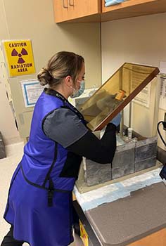 Woman examines specimen while wearing protective equipment. 