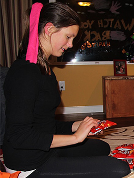 Girl kneeling on the floor and looking down at a packet of candy she is holding.