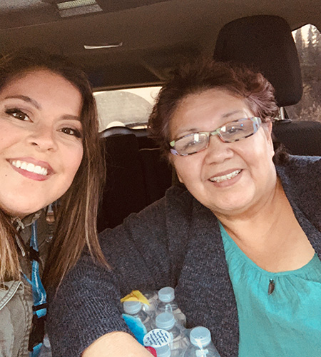 Two smiling women pose for a selfie inside a vehicle.