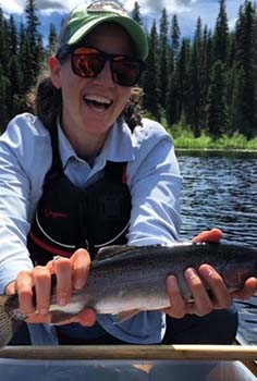 a woman smiles at the camera while on a boat, holding a fish, and wearing a PFD