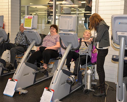 Patients on exercise bicycles at the YMCA monitored by physiotherapist.