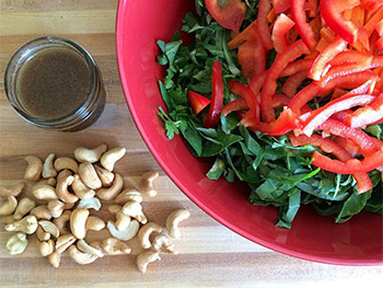 Portuguese kale salad in a red bowl with nuts and dressing on the side