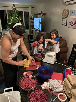 Man and two young children preparing and packaging ground meat  