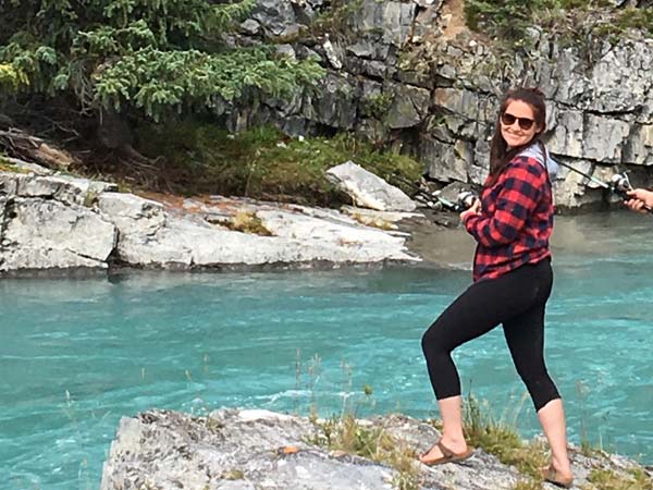 Shannon standing on a cliff above the river with a fishing pole.