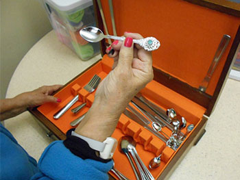 Woman's hand holding a silver spoon over a cutlery set