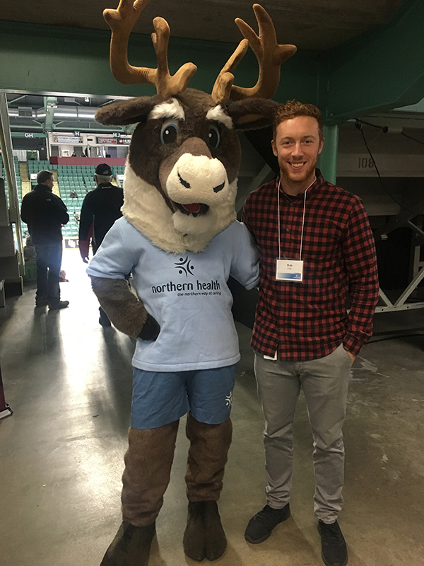 Spirit the mascot and a smiling young man wearing a red and black checked shirt.