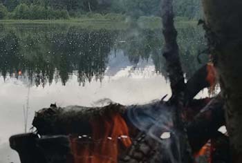 a fire in the front and in the back you can see a lake with a mountain and trees in the distance