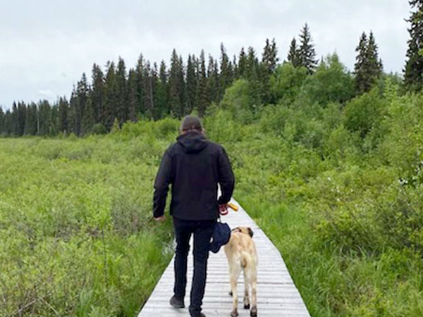 A man and a dog walk along a board walk on a lake.