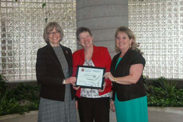 A woman with a plaque award stands between tow other women.