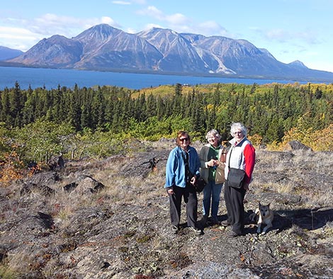 threee elderly ladies standing on a rocky outcrop with mountains and lake behind