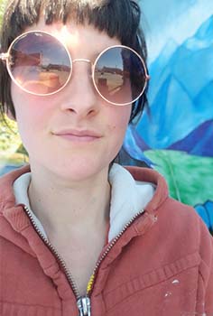 a girls with brown hair and large round sunglasses looks into the camera