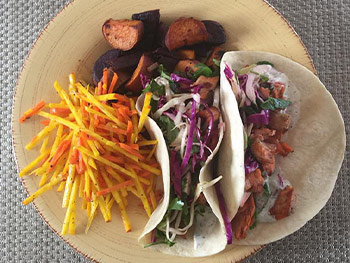 2 tacos on a plate with vegetables and fish.