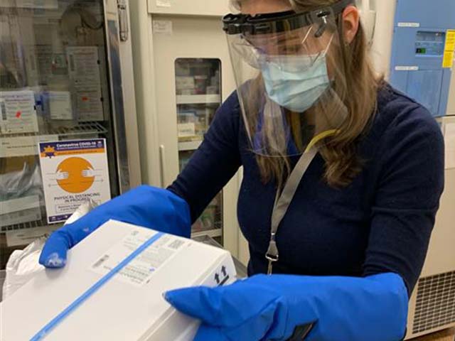 a woman in PPE holds a box of vaccines