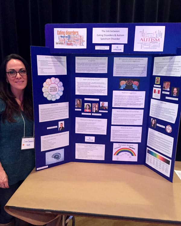 A woman stands beside a trifold presentation board.