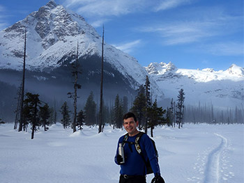 Man walking in the snow in front of a mountain background.