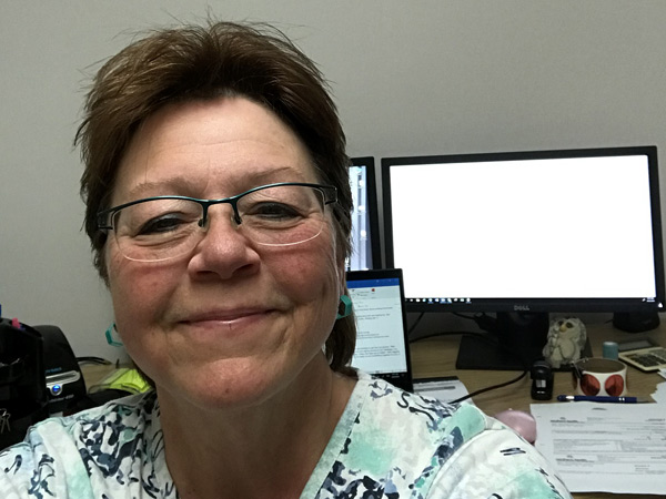 A woman smiles into the camera, her home office behind her. 