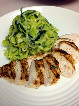 Sliced grilled chicken served on white plate with zucchini noodles