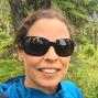 Woman with hair tied back and sunglasses outside in the forest.