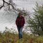 Woman with hat stands in front of lake. 