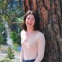 Woman with shoulder length brown hair stands against a tree trunk. 