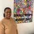Woman stands next to a colourful piece of artwork that reads "Small Steps every day"