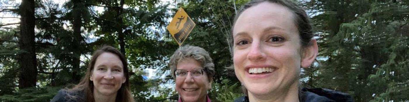 Three women smiling with green trees in the background