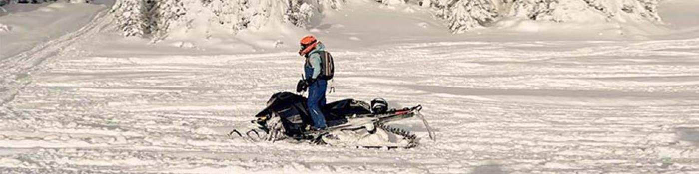 Snowmobile rider on snowy ground with trees