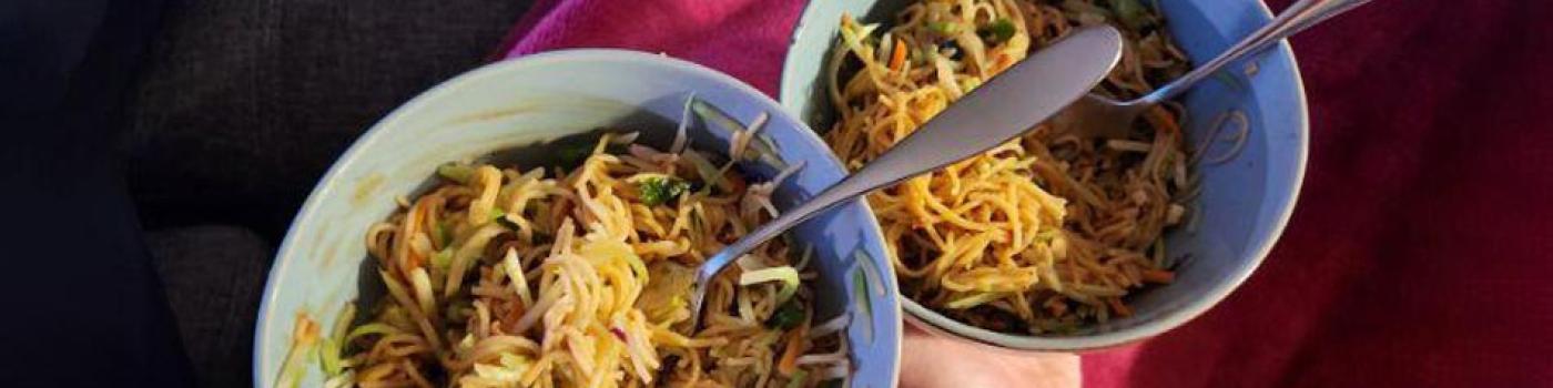 Hands holding bowls full of noodles