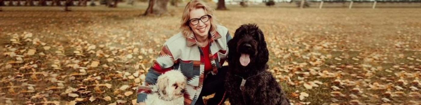 Woman with her two dogs and the ground is covered in yellow leaves.