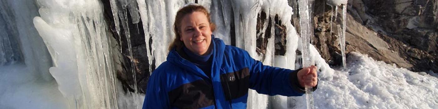 Penelope standing under a frozen waterfall wearing a blue jacket