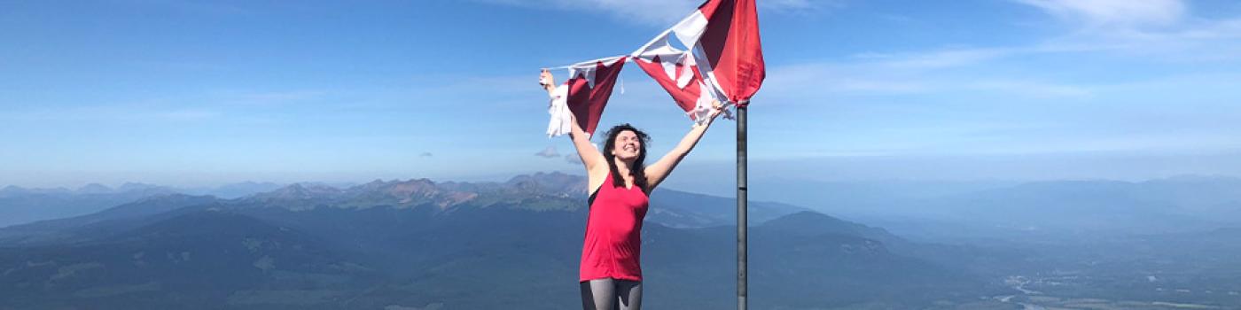 Savana standing atop a mountain holding a Canadian flag above her head