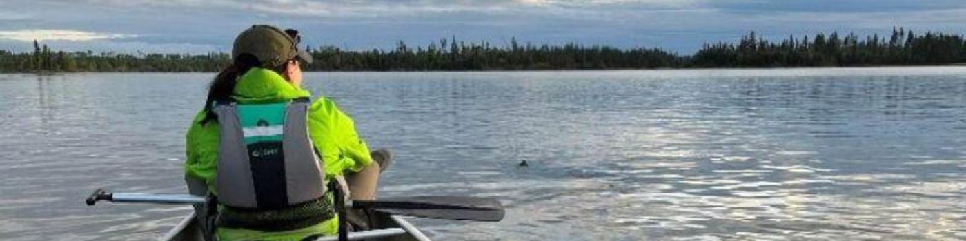 Woman sits at the front seat of a canoe in the water