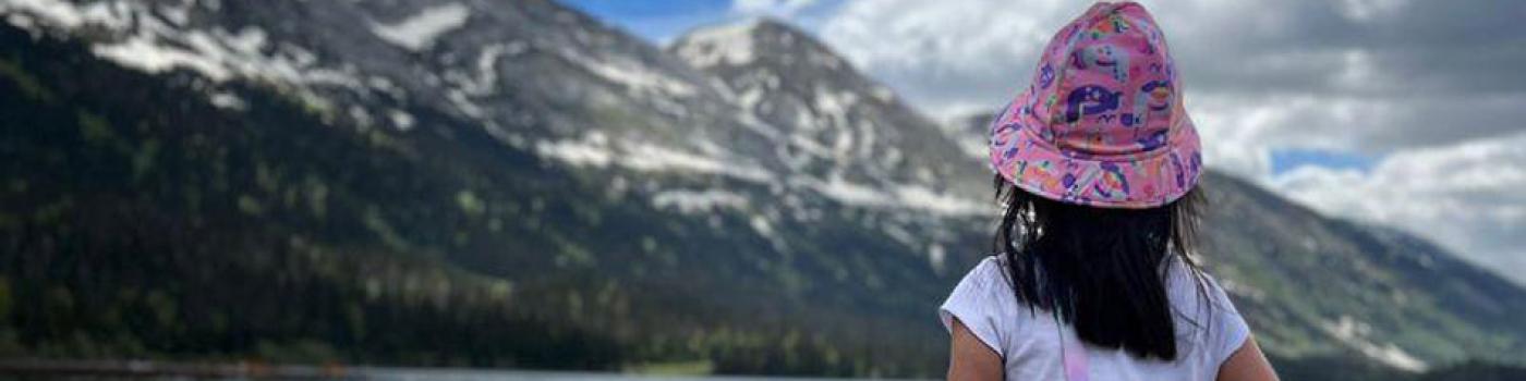 A child wearing a pink bucket hat looks out over a lake