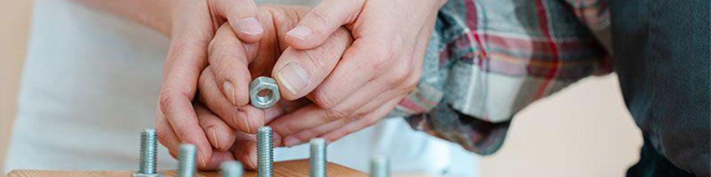 Two hands attempting to screw nuts onto protruding bolts.