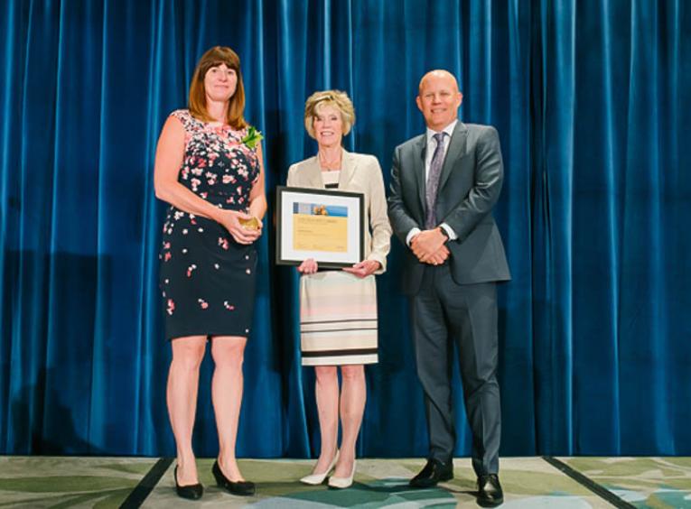 Woman standing on a stage between a man and another woman holding an award certificate