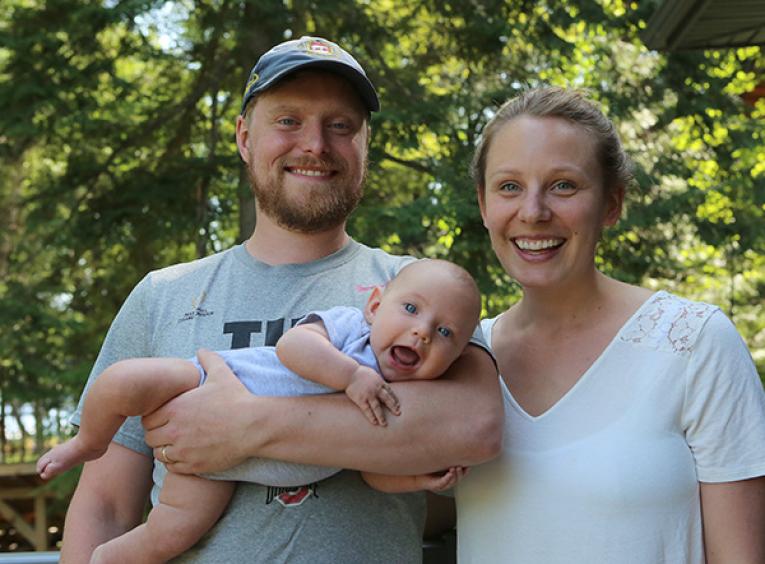 Dr. Jamie Wilkie and a woman stand beside each other outdoors. Dr. Wilkie holds a toddler.