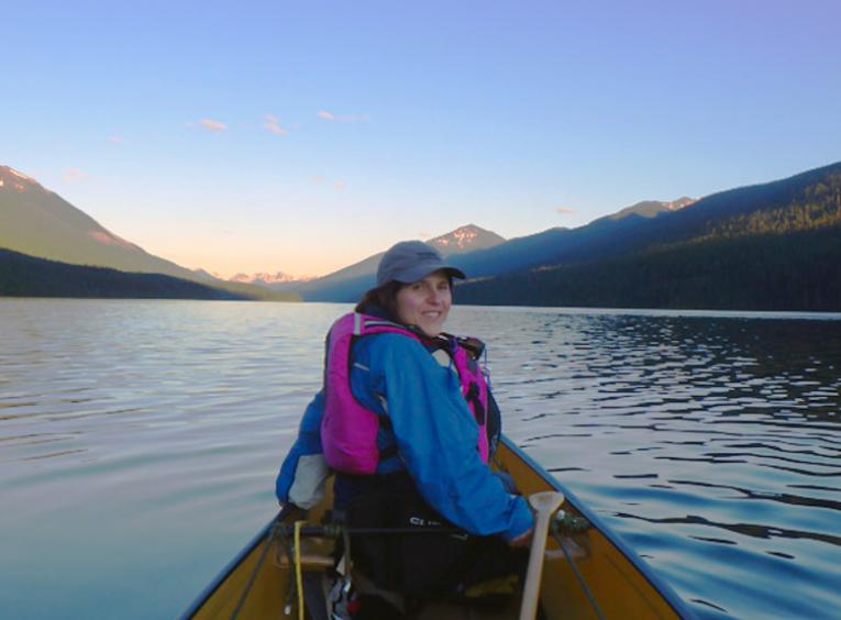 Ibolya is in the front of a canoe on a clam lake, surrounded by mountains.