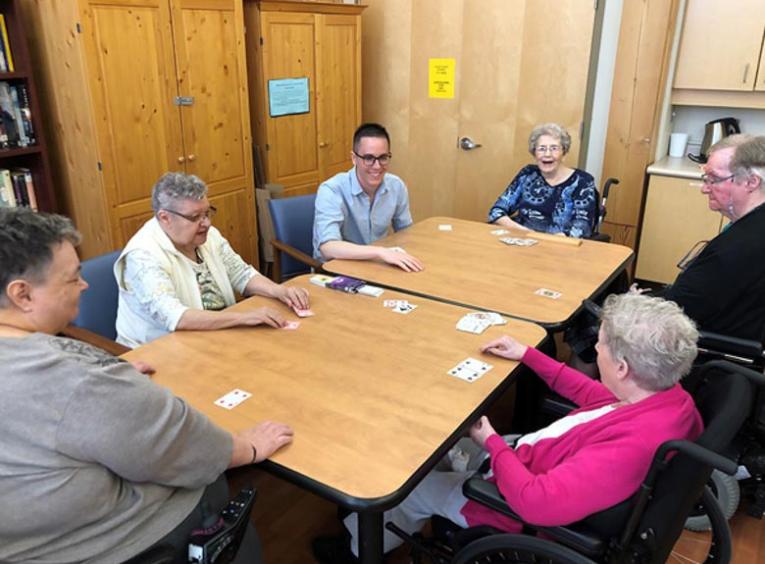 Zach, a young man, plays cards with five seniors.