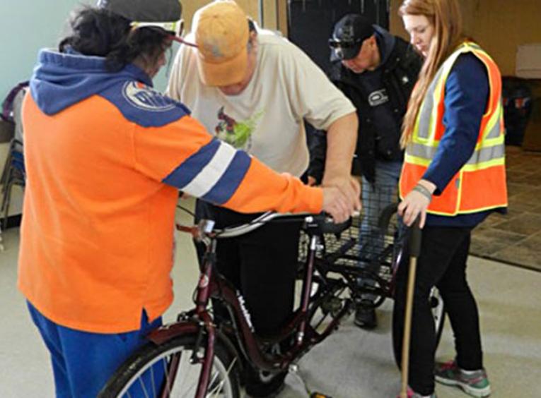 Staff supporting elder on a bicycle.