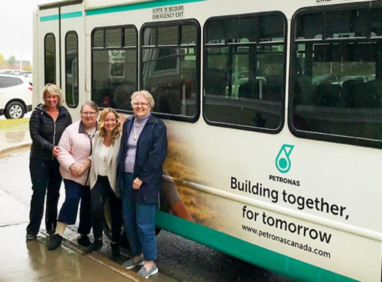 Four women stand in front of the new PETRONAS Canada shuttle bus for Peace Villa.
