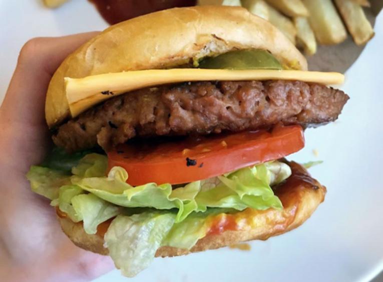 A hand holds a meaty-looking plant-based burger.