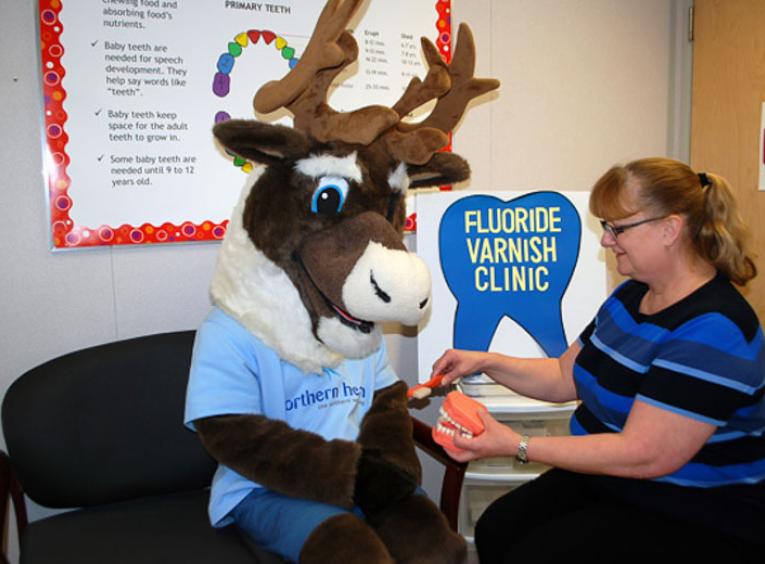 Spirit the Cariboo at a fluoride varnish clinic with an NH staff member.